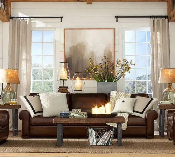 A person placing a light slipcover over a dark brown couch in a living room.