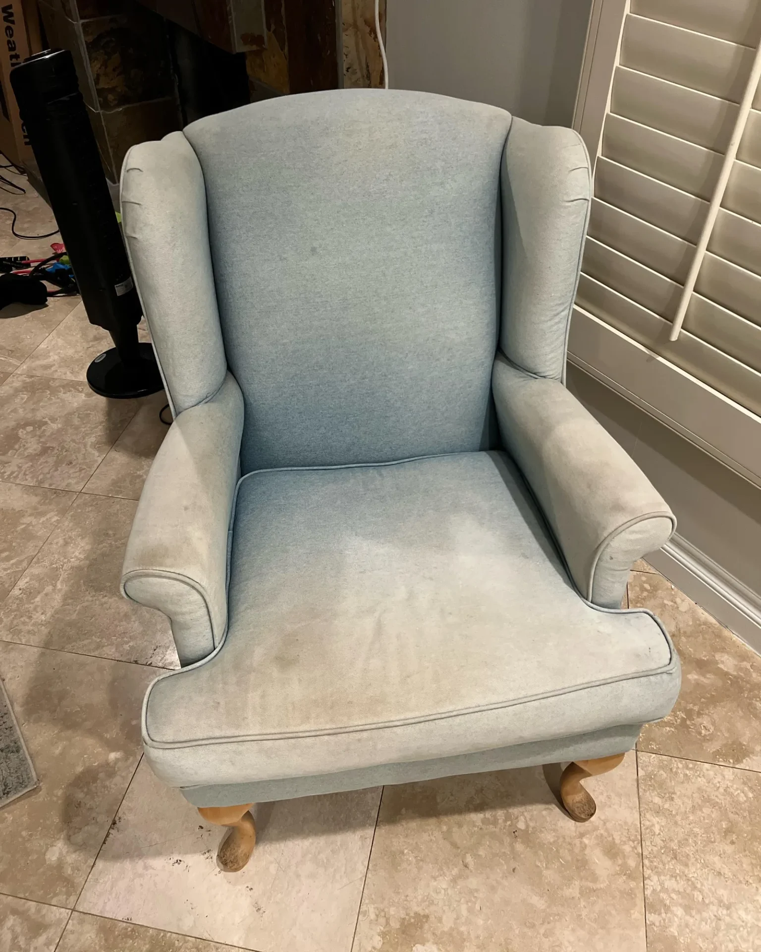 Professional hands using a staple gun on a tufted chair during the reupholstery process.